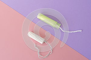 Two cotton tampons with light green applicator and without applicator on a pink and violet background. Hygienic types of tampons.