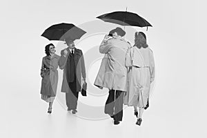 Two couple in elegant cloches, trench coats walking under umbrella. Monochrome image. Couple greeting photo