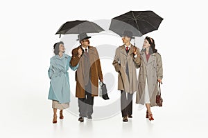 Two couple in elegant cloches, trench coats walking under umbrella, talking. Cheerful walk with friends. photo