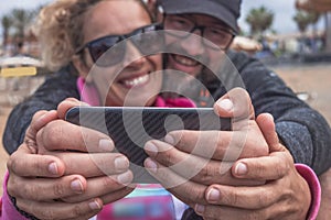 Two couple of hands of a middle-aged couple holding the mobile phone and smile for a selfie. Two attractive and relaxed people.