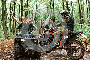 Two couples on ATV with man that is on the bike in the forest that looking at the camera