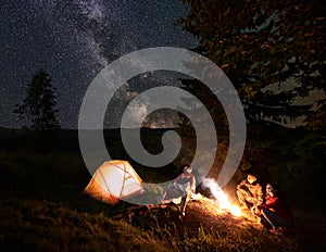 Two couples near campfire at night in the woods enjoying starry sky