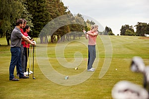 Two Couples Golfing Hitting Tee Shot Along Fairway With Driver With Clubs In Foreground