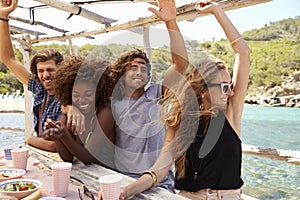 Two couples in a row at a table by the sea looking to camera