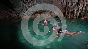 Two courageous girls are swimming in breathtaking cave pool, exploring amazing underground lake with transparent water