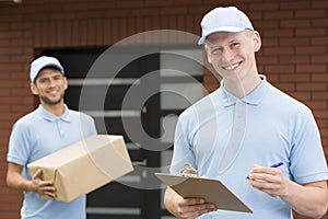 Two couriers in blue uniforms standing in front of a house and waiting with delivery