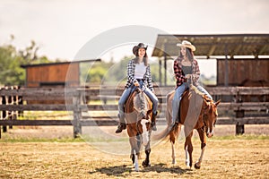 Two cowgirls riding their horses on a ranch during hot summer day