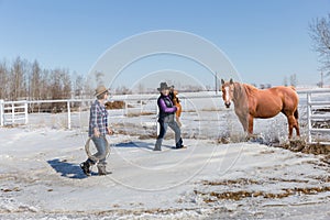 Two cowgirls walking with saddle toward horse to saddle up