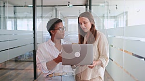 Two coworkers chatting during coffee break standing in glass hall of office building