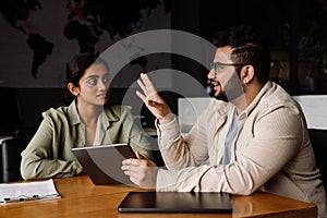 Two coworkers discussing business details and working on tablet while sitting in office