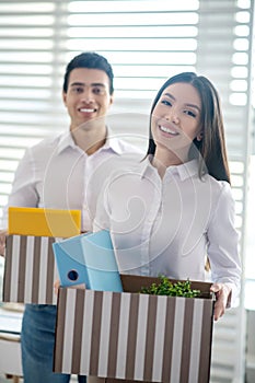 Two coworkers holding boxes with office stuff and feeling positive