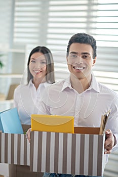 Two coworkers holding boxes with office stuff and smiling