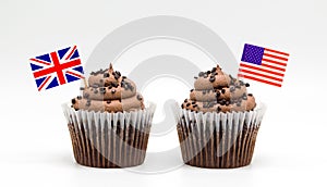 Two chocolate chip swirl cupcakes with tricolor American flag and British Union Jack flag toothpicks in them isolated on white