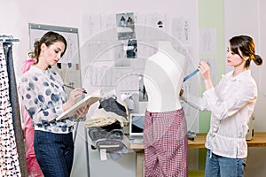 Two creative female seamstresses working in stylish atelier. Woman seamstress measuring mannequin, holding tape, while