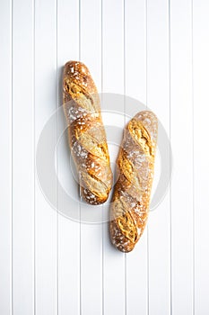 Two crispy fresh baguettes on white table