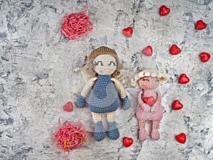 Two crocheted angels holding a decorative straw with pink hearts, a Valentine's Day card