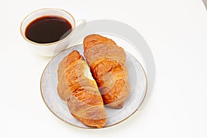 Two croissants on a white plate and a cup of black coffee on white table. Selective focus