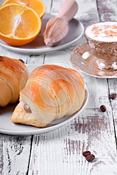 Two croissants of yeast dough on ceramic plate, freshly brewed coffee in a cup and oranges