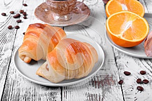 Two croissants of yeast dough on ceramic plate, freshly brewed coffee in a cup and oranges