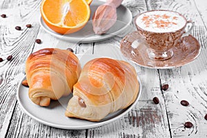 Two croissants of yeast dough on ceramic plate, freshly brewed coffee in a cup and oranges