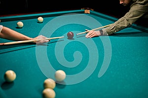 two cropped male playing snooker game or preparing aiming to shoot pool balls on billiard table