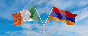 two crossed flags Armenia and Ireland waving in wind at cloudy sky. Concept of relationship, dialog, travelling between two