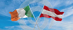 two crossed flags Austria and Ireland waving in wind at cloudy sky. Concept of relationship, dialog, travelling between two