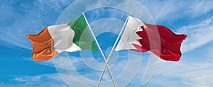 two crossed flags Bahrain and Ireland waving in wind at cloudy sky. Concept of relationship, dialog, travelling between two