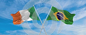 two crossed flags Brazil and Ireland waving in wind at cloudy sky. Concept of relationship, dialog, travelling between two