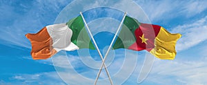 two crossed flags Cameroon and Ireland waving in wind at cloudy sky. Concept of relationship, dialog, travelling between two