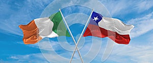 two crossed flags Chile and Ireland waving in wind at cloudy sky. Concept of relationship, dialog, travelling between two