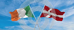 two crossed flags denmark and Ireland waving in wind at cloudy sky. Concept of relationship, dialog, travelling between two