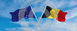 two crossed flags The European Union and Belgium waving in wind at cloudy sky. Concept of relationship, dialog, travelling between