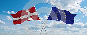 two crossed flags The European Union and Denmark waving in wind at cloudy sky. Concept of relationship, dialog, travelling between