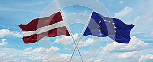 two crossed flags The European Union and Latvia waving in wind at cloudy sky. Concept of relationship, dialog, travelling between