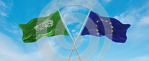 two crossed flags The European Union and Saudi Arabia waving in wind at cloudy sky. Concept of relationship, dialog, travelling