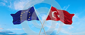 two crossed flags The European Union and Turkey waving in wind at cloudy sky. Concept of relationship, dialog, travelling between