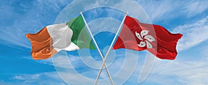 two crossed flags Hong Kong and Ireland waving in wind at cloudy sky. Concept of relationship, dialog, travelling between two