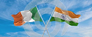 two crossed flags India and Ireland waving in wind at cloudy sky. Concept of relationship, dialog, travelling between two