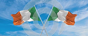 two crossed flags Ireland and Ireland waving in wind at cloudy sky. Concept of relationship, dialog, travelling between two