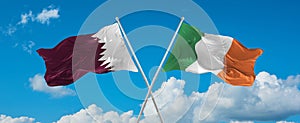 two crossed flags Ireland and Qatar waving in wind at cloudy sky. Concept of relationship, dialog, travelling between two