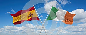 two crossed flags Ireland and spain waving in wind at cloudy sky. Concept of relationship, dialog, travelling between two