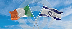 two crossed flags Israel and Ireland waving in wind at cloudy sky. Concept of relationship, dialog, travelling between two