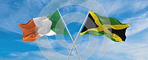 two crossed flags Jamaica and Ireland waving in wind at cloudy sky. Concept of relationship, dialog, travelling between two
