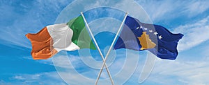 two crossed flags Kosovo and Ireland waving in wind at cloudy sky. Concept of relationship, dialog, travelling between two