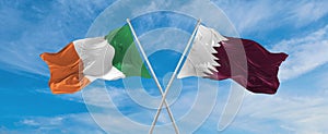 two crossed flags Qatar and Ireland waving in wind at cloudy sky. Concept of relationship, dialog, travelling between two