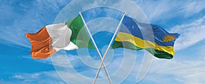 two crossed flags Rwanda and Ireland waving in wind at cloudy sky. Concept of relationship, dialog, travelling between two