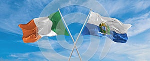 two crossed flags San Marino and Ireland waving in wind at cloudy sky. Concept of relationship, dialog, travelling between two