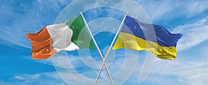two crossed flags Ukraine and Ireland waving in wind at cloudy sky. Concept of relationship, dialog, travelling between two