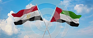 two crossed flags United Arab Emirates and Egypt waving in wind at cloudy sky. Concept of relationship, dialog, travelling between